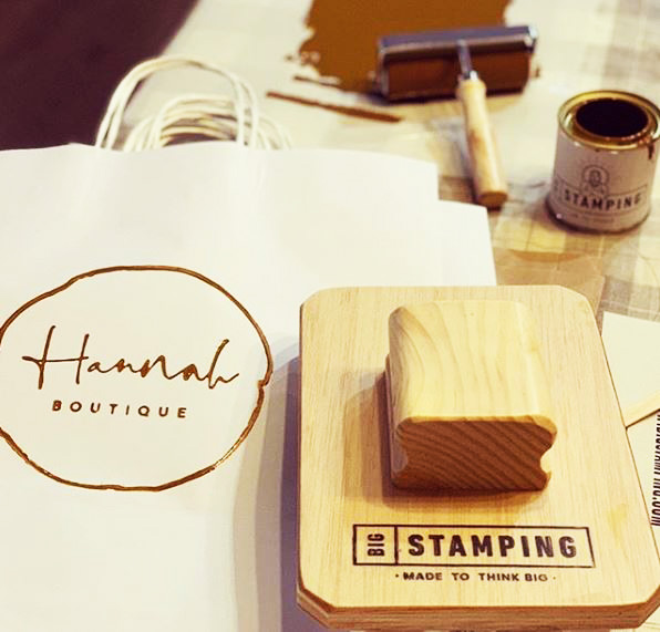 Un sello BigStamping personalizando una bolsa de papel blanca